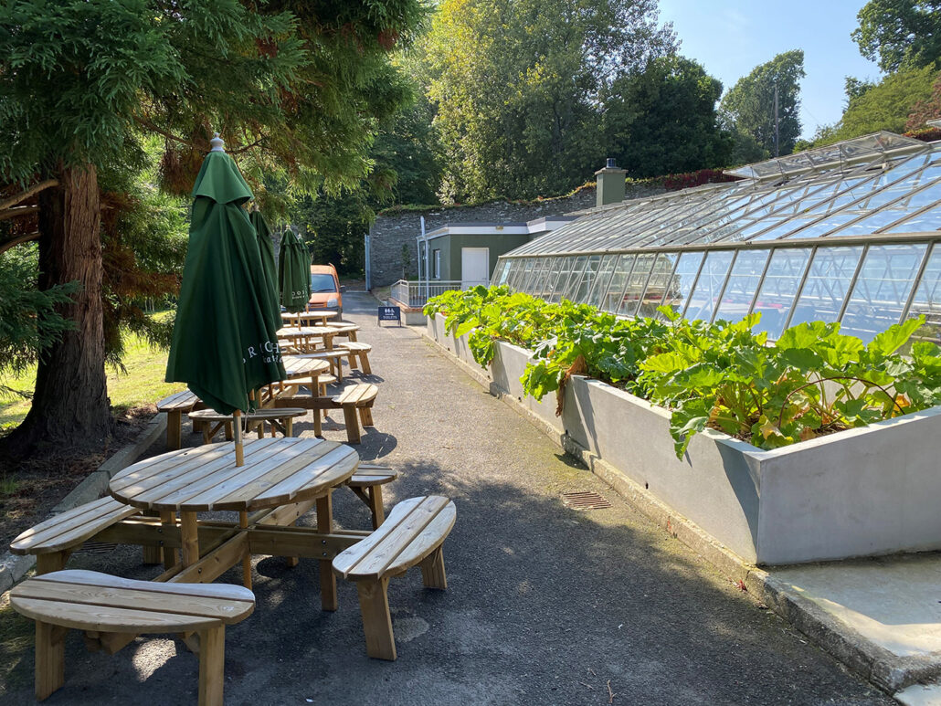 view of the green house at brook hall flanked by benches on a beautiful sunny day